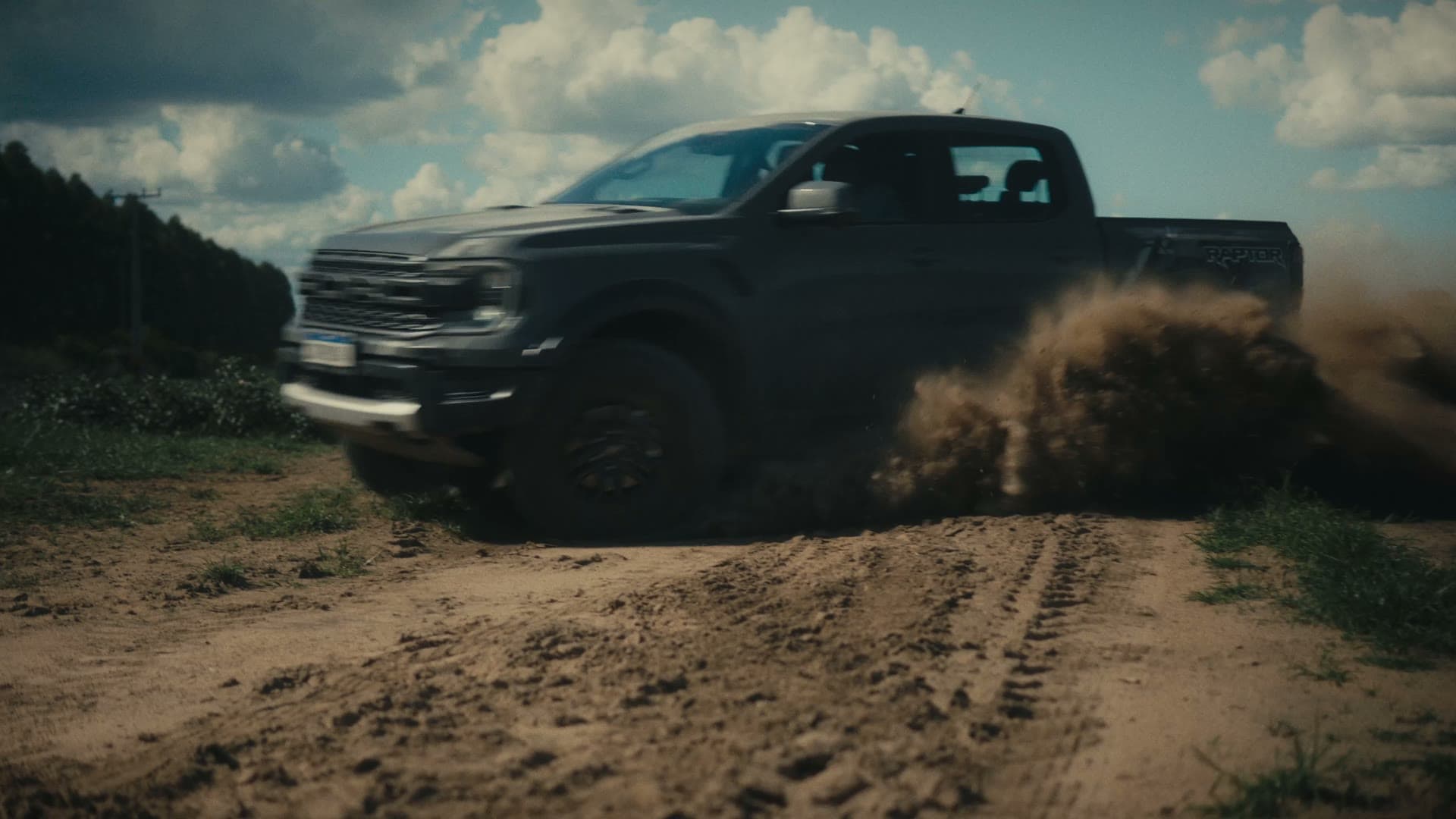 Picape Ford Ranger derrapando em estrada de terra, levantando poeira sob céu com nuvens.